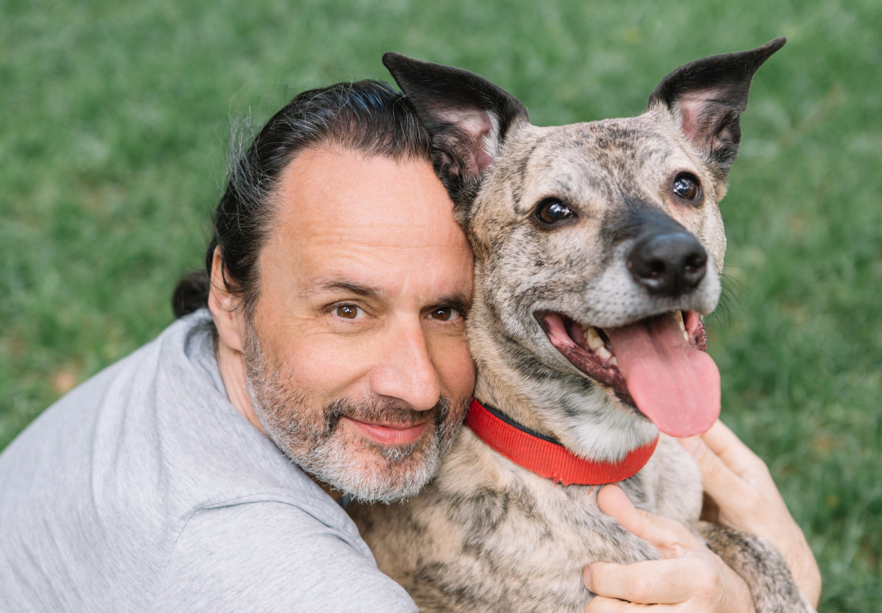 A man sitting on grass while hugging a dog.